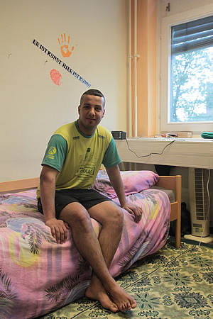 Amer sitting on the edge of the bed (KUNSTASYL ©caveng)